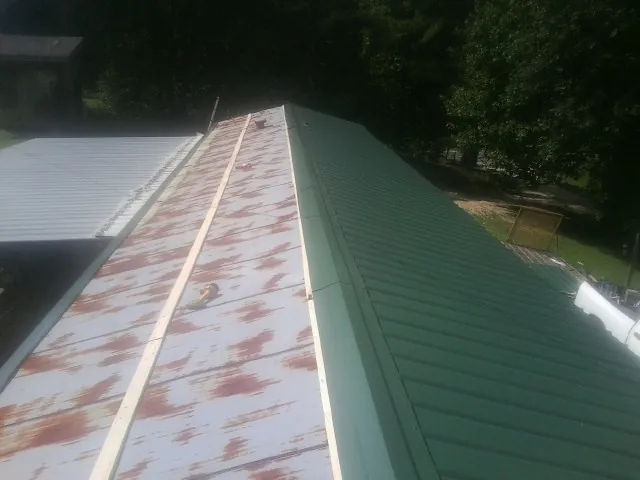 Old rusted panels beside newly installed green metal roofing — Wind Damage Roof Repair by Roofing Brothers in Cape Charles
