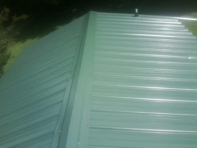 New green metal panels meeting at the ridge of a roof — Flat Roof Repair work by our crew in Cape Charles